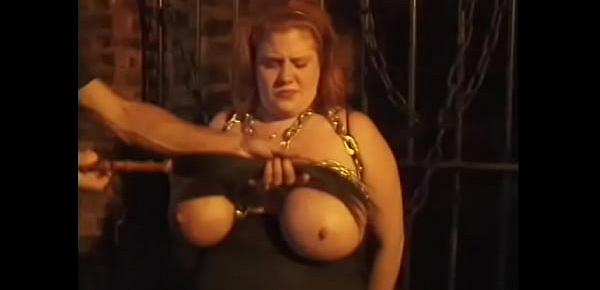  Horny executioner ties up sexy redhead whore and hangs chains on her huge cans